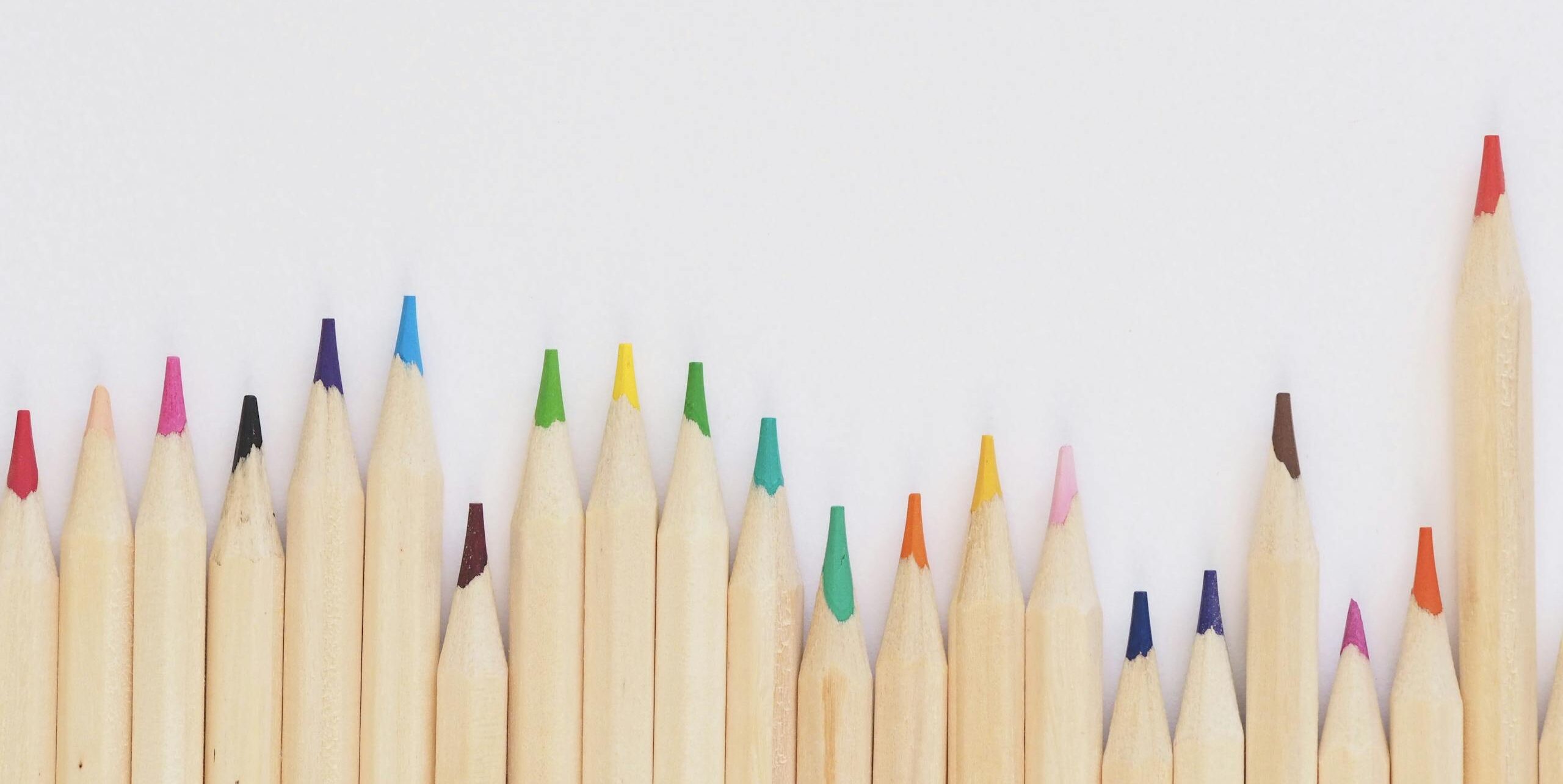 A row of vibrant colored pencils aligned on a white background, providing ample copyspace.